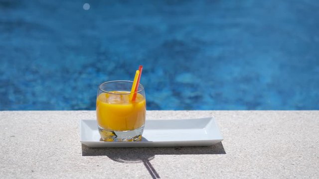 Two glasses with tropical, mango, orange juice with ice cubes on outdoor swimming pool or sea background. Happy woman takes one glass for drinking. Summer luxury drink.