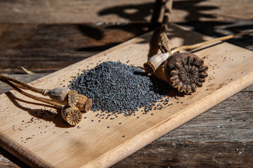 Poppy seeds and dried poppy heads on a wooden board on the kitchen table.