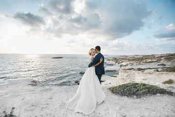 Newlywed couple hugging together on the white rocks at the seacoast at Cyprus. The bride in a...