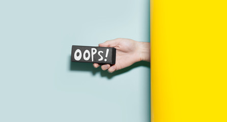 Close-up of male hand holding a small black board with oops definition, between two backgrounds of yellow and aqua menthe color.
