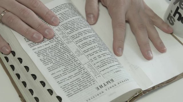 A man puts a beautiful Bible in front of him, opens it and is going to make notes with an orange marker, which he holds in his hand. Close-up shot
