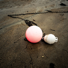 Close-up view of a pink and a white buoy and their anchorage chains, lying on the wet sand on the...