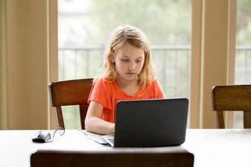 A young girl does school work at home on a laptop computer