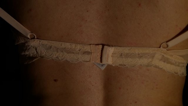 Woman in the dark takes off a beige bra