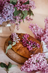 Homemade Apple pie on a wooden table next to a bowl of lilacs. Gentle toning.