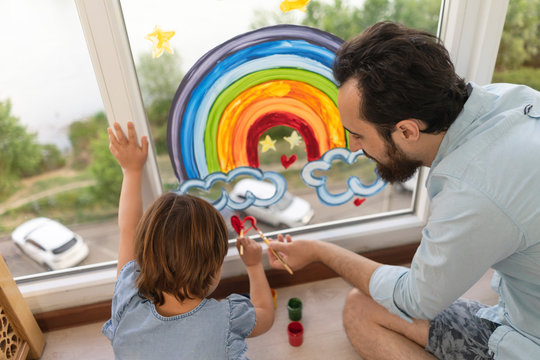 Father and daughter is arts draw on the window rainbow and hearts. Family fun, interesting creative activities and games with children.