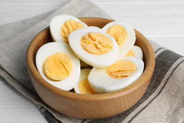 Cut hard boiled chicken eggs in wooden bowl on table