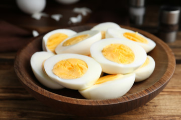 Cut hard boiled chicken eggs in wooden bowl on table