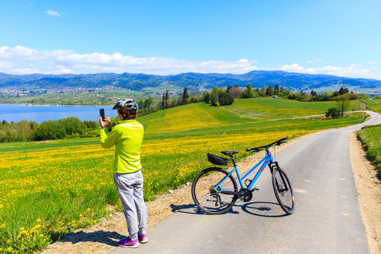 Woman cyclist taking picture with phone of Czorsztynskie lake near Falsztyn village on sunny spring day, Pieniny Mountains, Poland
