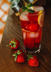 Fresh cold lemonade with strawberries and lemon on wooden background. Citric, healthy