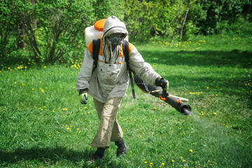 A worker in a protective suit carries out chemical and sanitary treatment in a garden or park....
