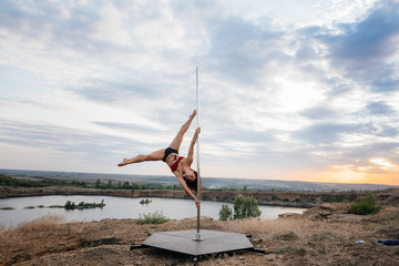 A young sexy girl performs amazing exercises on a pole during a beautiful sunset. Dance. Sexuality