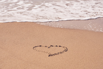 A heart symbol written on a sandy beach with foam and water background. Valentines day concept.