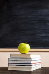 Books, apple, pens, pencils and glasses on a wooden table, against the background of a chalk board. Concept for Teacher's Day, copy space.