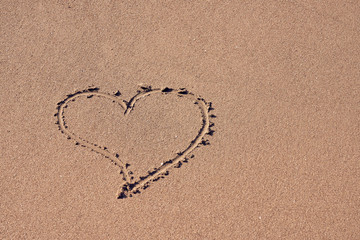 A heart symbol written on a sandy beach with foam and water background. Valentines day concept.