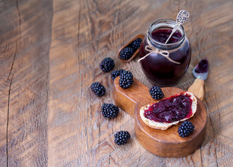 Blackberry jam toast and homemade blackberry jam in glass jar with fresh berries. Wooden background, selective focus, copy space.