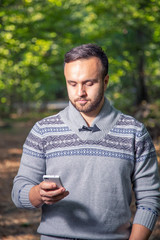 Fototapeta premium Portrait of handsome adult man sending a text message while standing in the city park