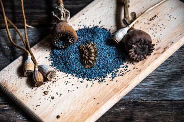 Poppy seeds and dried poppy heads on a wooden board on the kitchen table.