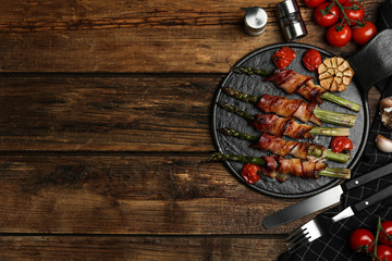 Oven baked asparagus wrapped with bacon on wooden table, flat lay. Space for text