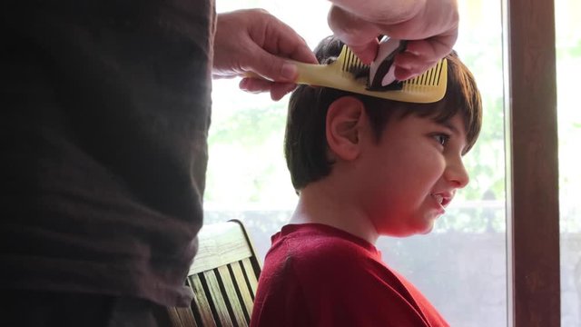 Hair cutting at home. Epidemic of coronavirus infection COVID-19. Hairdressers are closed.A serious child on a haircut by dad. A boy in red clothes is scissored by cutting bangs on his head.