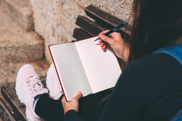 Young woman sits on bench in park with blank notebook and pen on her hands. Wish Marathon. Writing wishes and dreams in a notebook. Life with a clean slate. Space for text. Thoughts about your desires