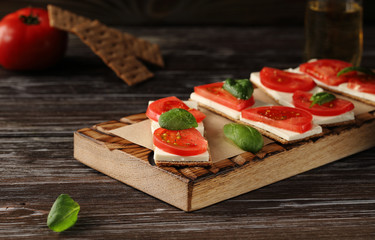 Crispbread with feta cheese, red tomatoes and mini spinach leaves, on a wooden board, with a glass of white wine. Delicious and light small sandwiches.