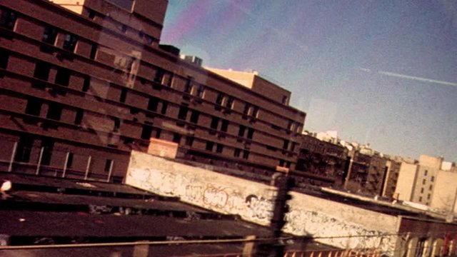 Retro looking archival footage filmed on New York City subway looking out through subway window at tracks and passing train with apartments and graffiti in the distance