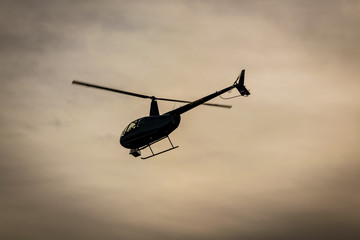 Black helicopter departing against yellow sky