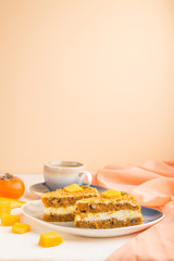 Homemade cake with persimmon and pumpkin and a cup of coffee on a white and orange background with orange textile. side view, copy space.