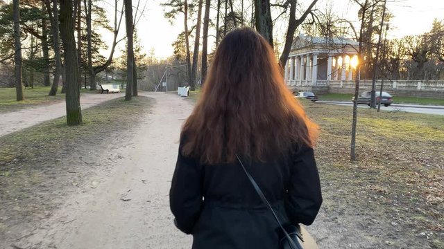 Walking POV rear view of woman walking down footpath in Marienthal park, Pavlovsk in the evening, Saint Petersburg, Russia.