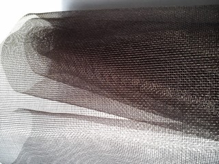 Mosquito net in a roll. Brown synthetic material on a white background. Weaving plastic threads....