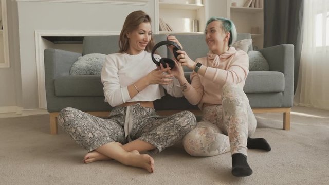Girl sharing music with friend using wireless ear buds at home.