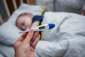 An electronic thermometer without mercury shows nothing. In the background, a sleeping child in a crib.