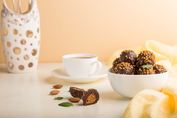Chocolate caramel ball candies with almonds and a cup of coffee on a white and orange background. Side view, copy space.