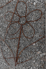 A flower made of rusty rebar on a background of stones.