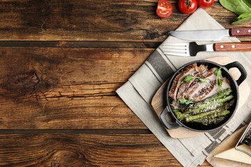Tasty meat served with asparagus and sprouts in portioned frying pan on wooden table, flat lay. Space for text