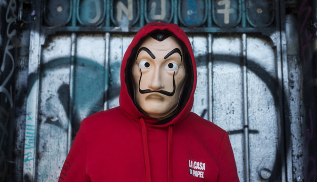 Mulhouse - France - 18 May 2020 - fan of "La casa de papel" (paper house) in english the serie TV on Netflix, standing with red sweat shirt costume and Salvador Dali mask on graffiti background