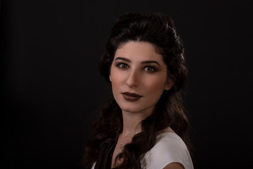 Close-up portrait of a archer woman in white dress on black background. Greek goddess Artemis. Studio photo shoot. Professional makeup and hairstyle for a brunette with long dark hair. Young woman