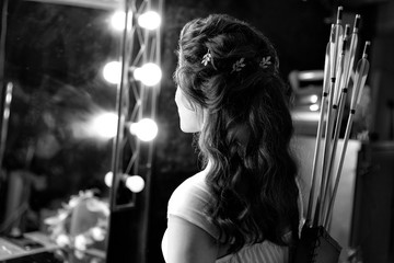 Black and white image of archer woman from back in white dress with bow and arrow on studio lights...