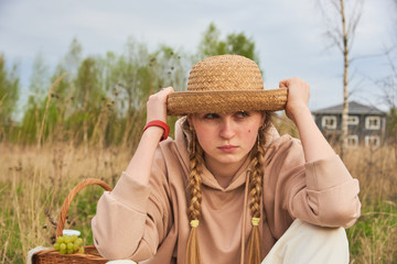 A teenage girl pulled a straw hat over her eyes sits in a field .