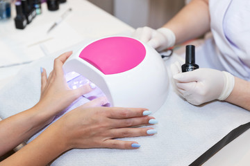 Close-up beautiful woman hands and lamp for nails on table. Nail gel salon. UV lamp. Process of...