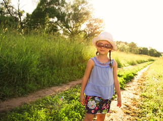 Beautiful long hair fun kid girl enjoying green grass summer sunny day background in fashion sunglasses and hat. Closeup