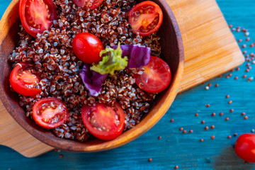 Red quinoa salad with tomato on a rustic table. Superfood and healthy eating concept.