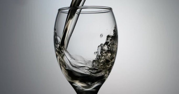 Closeup shot of glass being filled up with stream of alchoholic white wine in slow motion, pouring beverage into goblet, isolated on white background