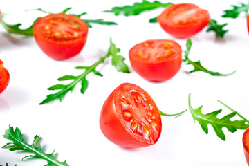 Halved red cherry tomatoes with green rucola leaves isolated on a white background.