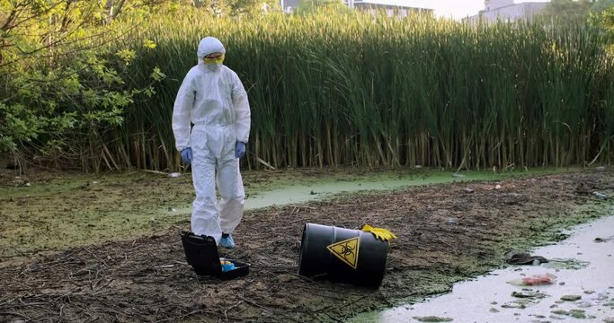 A scientist in a protective suit comes to a barrel with a sign of biological danger after a technological accident.