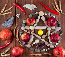 Pentagram made of stones with pomegranates, apples, dry ears and red hot chili peppers on a wooden...