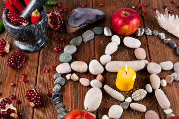 Pentagram made of stones with pomegranate, apples and red hot chili peppers on a wooden background.