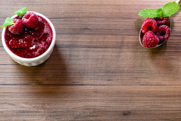 Spoon with raspberry and bowl with raspberry jam on wooden background