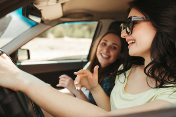 Obraz na płótnie Canvas Young joyful women friends having fun traveling by car. Tourism lifestyle, friendship and travel concept